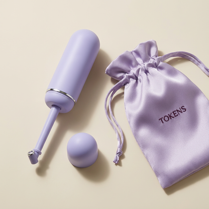 Lavender portable bidet beside a Tokens-branded silk drawstring bag, packaging concept